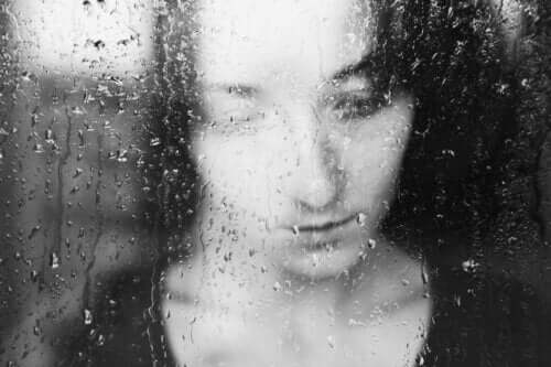 Kvinde kigger ud af regnfyldt vindue