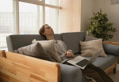 Ung fyr, der sover i sofa med bærbar på skødet