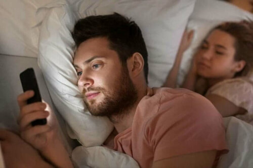 Par i seng, hvor manden bruger telefonen til digitalt utroskab