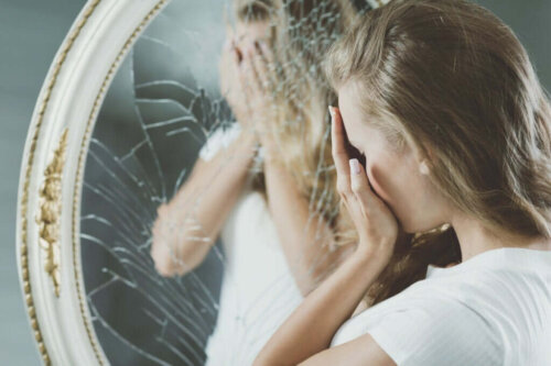 Kvinde gemmer ansigt i hænderne foran ødelagt spejl på grund af æstetiske besættelser