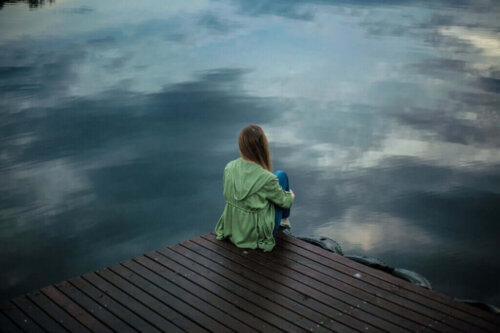 Kvinde sidder på bro ved sø