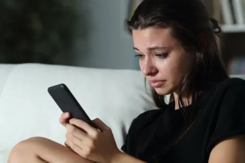 Kvinde med telefon i hånden græder på grund af ghosting blandt venner
