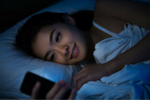 Kvinde ligger med telefon i sengen