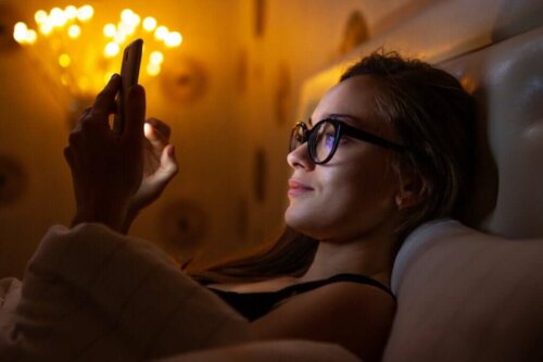 Kvinde ligger i sengen med telefon