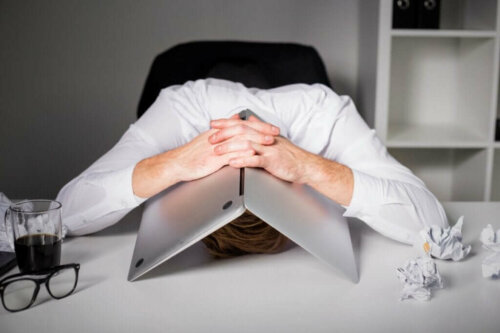 Mand med arbejdsstress gemmer hoved under computer