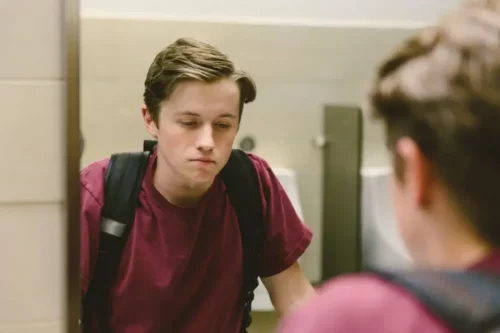 Trist ung mand ser sig i spejl og illustrerer behovet for at hjælpe teenagere med at overvinde problemer med deres image