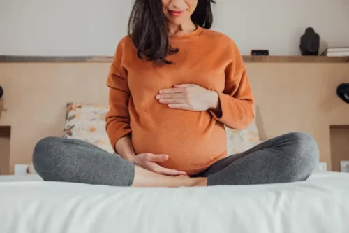 Gravid kvinde sidder på seng