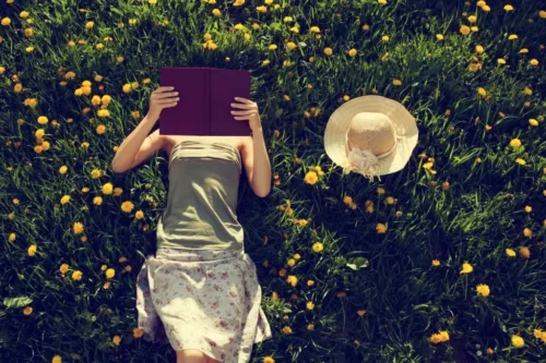 Kvinde læser bog liggende på græs