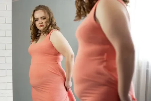 Overvægtig kvinde ser sig i spejlet
