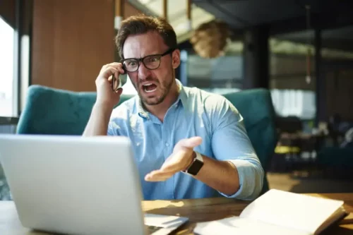 Mand, der snakker i telefon, råber af sin computer