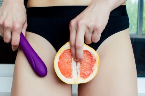 Kvinde står med dildoer og appelsin foran underliv