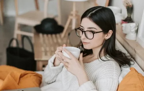 Kvinde med en kop te sidder i sofa og tænker