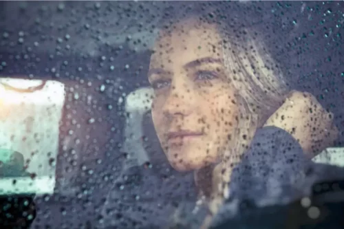 Kvinde bag vindue med regn ser det bittersøde i livet