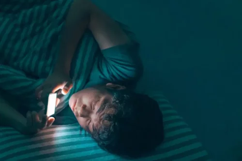 Barn ligger i seng med en telefon