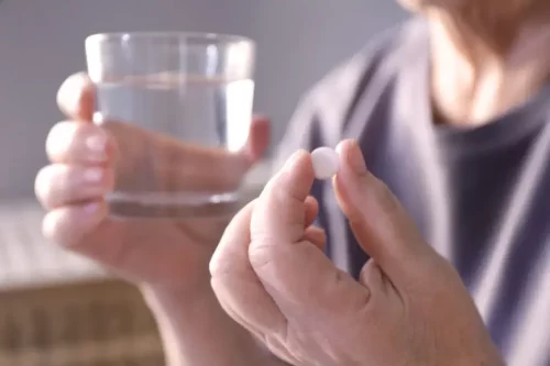 En person holder en pille og et glas vand