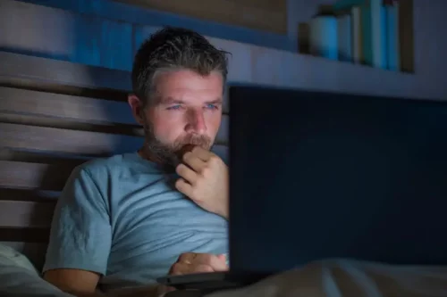 Træt mand ser på computer i seng som eksempel på brug af porno