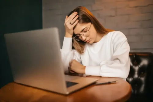 Træt kvinde ved computer oplever, hvordan faktorer i arbejdsmiljøet kan påvirke en negativt