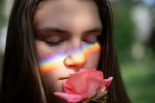 Kvinde med regnbue foran ansigtet dufter til rose