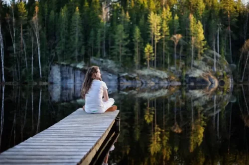 Kvinde sidder på bro ved sø