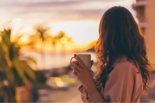 Kvinde nyder solopgang med en kaffekop i hånden