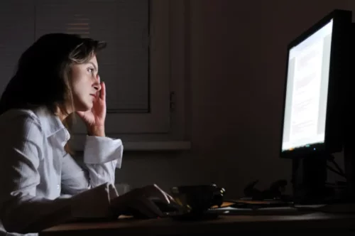 Kvinde ved computer i mørke er ved at besvare arbejdsmails