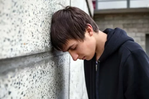 Trist ung mand, der er vokset op i en dysfunktionel familie, hviler hovedet mod en mur