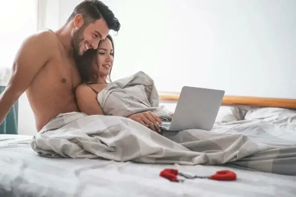 Nøgent par i en seng med en computer snakker om almindelige seksuelle fantasier